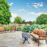 Well designed patio area with stone floor in the backyard of a yellow house. Relaxing area with comfortable outdoor furniture and blooming hydrangea flowers. Northwest, USA