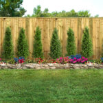 Empty backyard with green grass, trees, flowers and wood fence